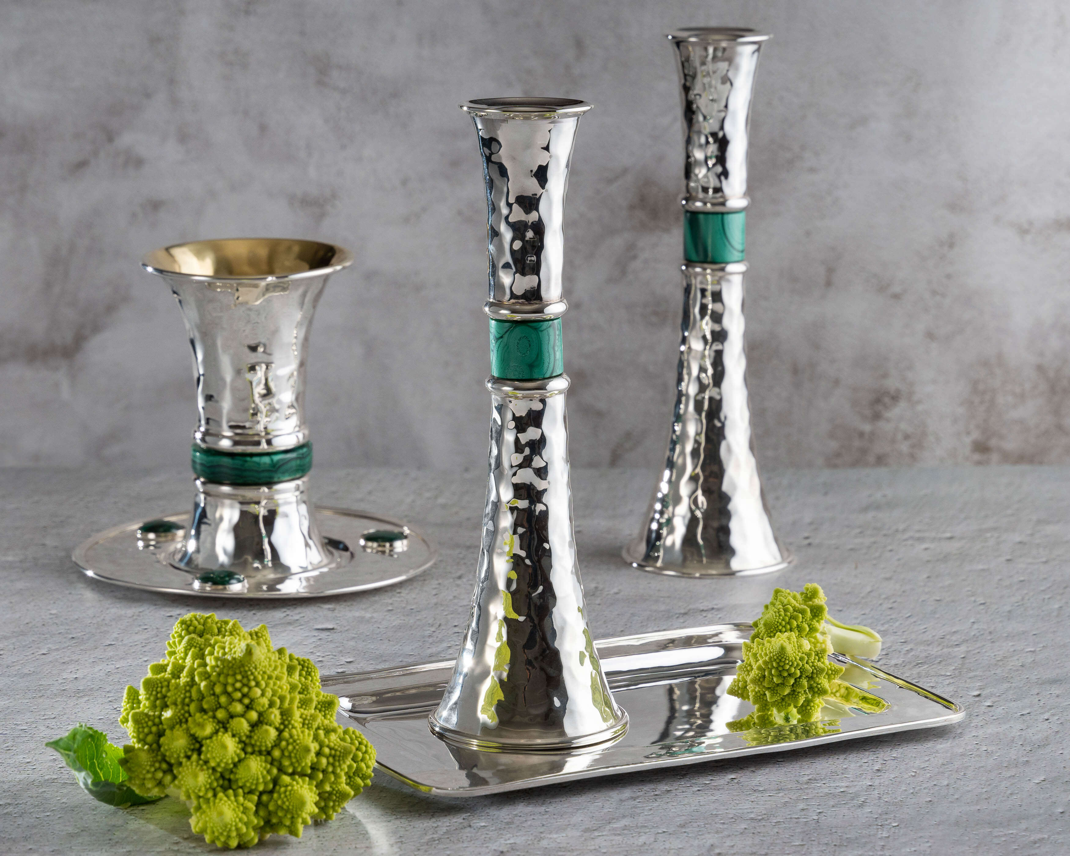 Set of silver candle holders with green ribbons on a gray surface with decorative green leaves.